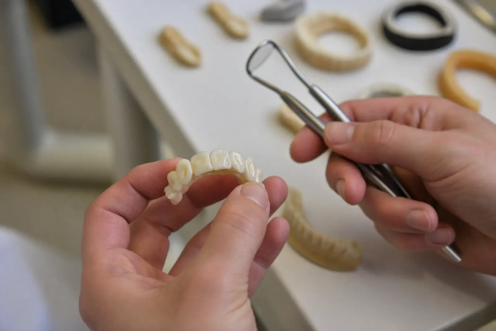 A dental technician's hands holding a set of porcelain teeth above a lab bench